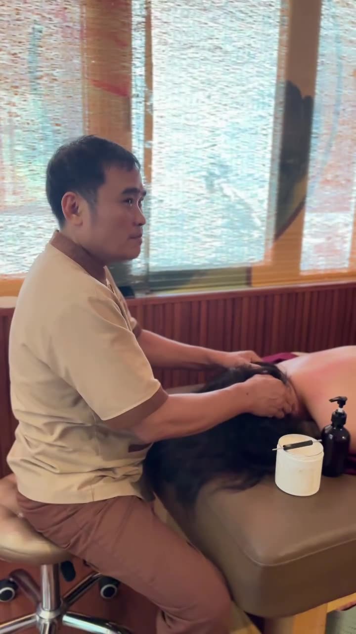 Male Tong Gia technician massaging a guest's head and turning to smile during a relaxing session